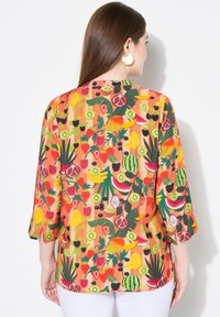 Blusa colorata a maniche corte con una vivace stampa di frutta in tonalità di arancione, verde, rosso e giallo, realizzata in tessuto leggero.