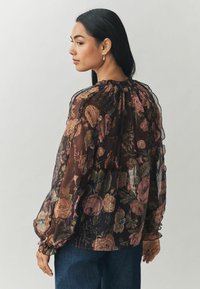 Permatomas juodas bluzonas su rožių raštu, kurio spalvos - rožinė ir mėlyna. Apima susirinkusią kaklo liniją ir elastingas rankoves, pagamintas iš laisvai krentant fabric.