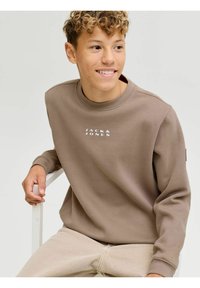 Sudadera marrón con cuello redondo y logo blanco de "JACK & JONES" en el pecho. Tejido suave, con un fondo neutro.