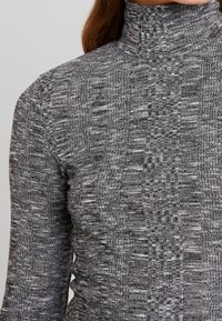 Harmaa, teksturoitu poolopaita, jossa istuva siluetti. Kangas on kudottu kuvio ja siinä on korkea kaulus lisäsuojaa varten.