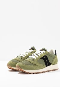 Tummanvihreät ja vaaleanvihreät mokkanahasta ja verkosta valmistetut tennarit, joissa on valkoiset nauhat, mustat yksityiskohdat ja vaaleanvärinen kumipohja. Logo kielekkeellä.