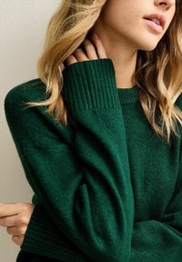 Groene trui met geribde manchetten en een ronde hals. Zachte textuur en een losse pasvorm zorgen voor een comfortabele uitstraling. Benadrukt het schoudergedeelte.