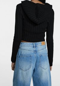 Svart ribbad kort hoodie med huva, kombinerad med ljusblå vida jeans i denim med bakfickor och en urtvättad finish.