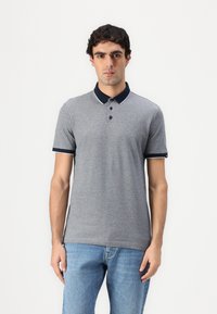 Siva polo majica s tamnoplavim ovratnikom i bijelim obrubom, s tri dugmeta. Uparena s svijetloplavim trapericama, kratki rukavi, glatka tekstura tkanine.