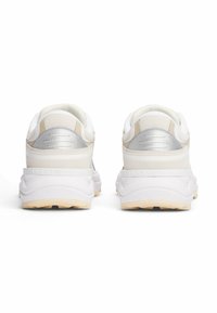 Witte sneakers met zilveren accenten, ronde achterkant, textuurmateriaal op de hak en een tan rubberen buitenzool met een grip patroon.