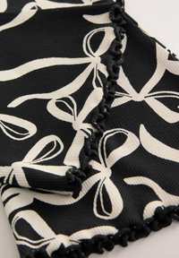 Black fabric with a white bow pattern; textured surface with a frilly black trim along the edges. Smooth and flexible design.