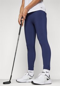 Navy blå leggings med en glat tekstur og tætsiddende design, parret med hvide træningssko med sorte detaljer og lange strømper.