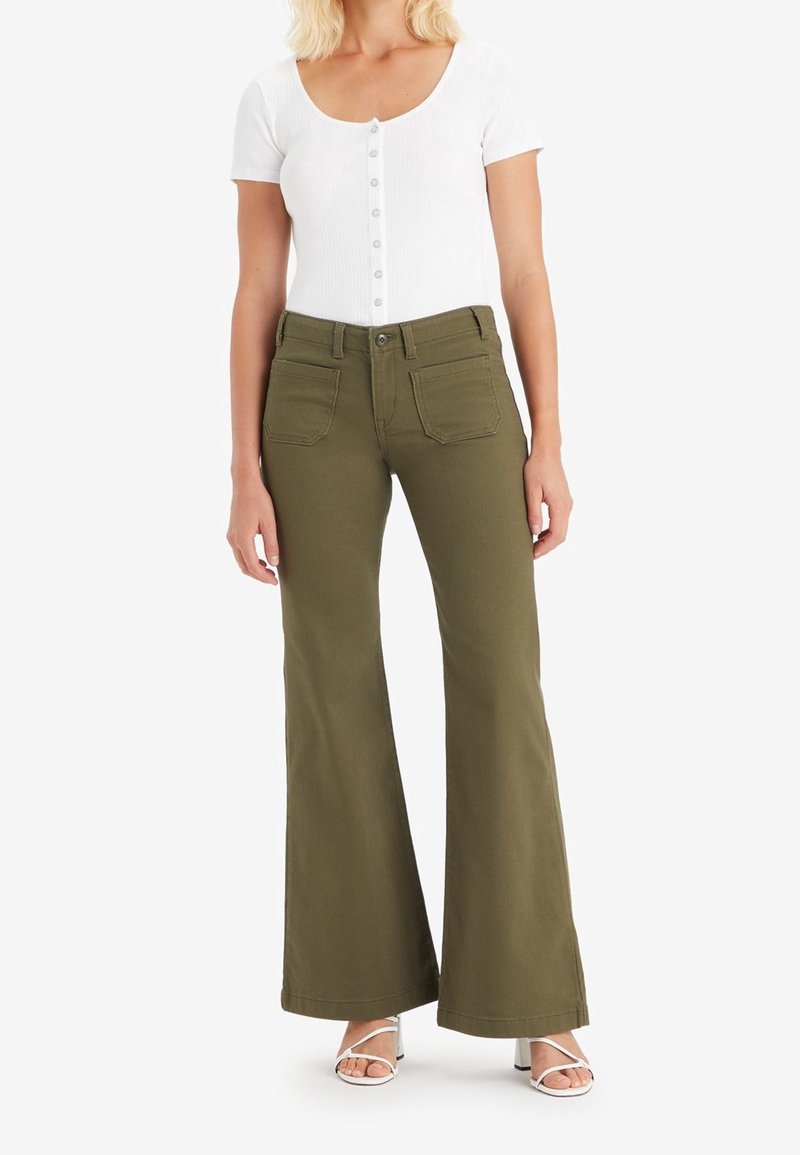 Pantalon évasé vert olive à taille haute avec deux poches arrière, associé à un haut blanc à manches courtes côtelé avec boutons.
