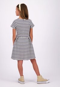 Gestreiftes Kleid mit kurzen Ärmeln in Marineblau und Creme, mit einem ausgestellten Rock und einem Reißverschluss auf der Rückseite. Kombiniert mit beigen High-Top-Sneakern.