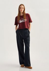 Krótkie, marsala t-shirt z białą grafiką "Manhattan"; połączone z szerokimi, ciemnoniebieskimi spodniami; brązowe buty; gładki materiał.