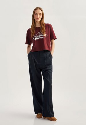 Bordeaux cropped t-shirt met witte "Manhattan" grafiek; gecombineerd met donkerblauwe wijde broek; bruine schoenen; gladde stof.