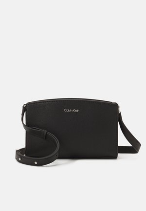 Zwarte crossbodytas van Calvin Klein met gestructureerd leer, verstelbare riem en zilveren logo centraal aan de voorkant.