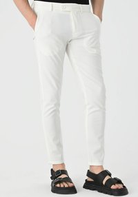 White slim-fit trousers made of lightweight fabric, featuring a flat front and side pockets, paired with chunky black sandals.