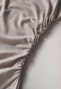 Tissu gris côtelé avec détail froncé, mettant en valeur une texture lisse et un éclat subtil. Les plis créent une apparence décontractée.