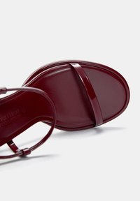 Burgundowe sandały z błyszczącej skóry, z minimalnymi paskami, płaską podeszwą i eleganckim designem, idealne do noszenia na co dzień.