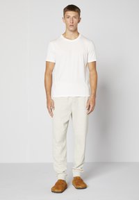 Vit crew-neck t-shirt, ljusgrå joggers och bruna slip-on skor. Joggers har en avslappnad passform med avslutade fållar. Släta bomullstyger.