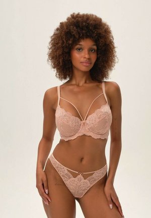 Lace lingerie set in soft pink featuring a detailed floral pattern, adjustable straps, and a cut-out design on the waistband.