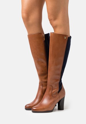 Bottes montantes en cuir marron avec panneaux en daim bleu marine, fermeture éclair et bout arrondi. Talon empilé offrant hauteur et stabilité.