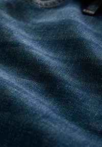 Sügavast indigovärvist denimpakend, millel on peen twiilitekstuur, kerge valguse kulumine ja pehme, veidi kortsus välimus.