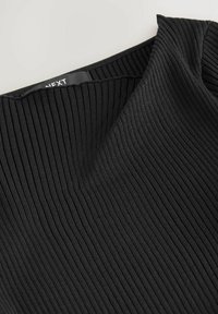 Prim-plan al unui material tricotat negru, cu un decolteu în V pliat și o etichetă parțial vizibilă în interiorul gulerului.