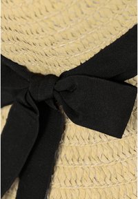 Cappello di paglia con una texture intrecciata, colore beige naturale e un ampio fiocco nero legato alla base.