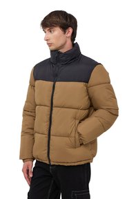 Giacca a vento con parte superiore nera e parte inferiore beige, dotata di cerniera frontale, colletto alto e due tasche laterali.