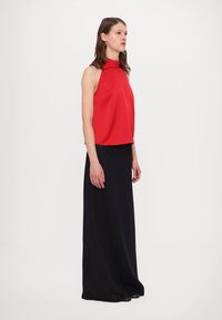 Haut halter rouge avec un col haut associé à une longue jupe noire, le tout en tissu lisse, créant une combinaison de couleurs contrastées.