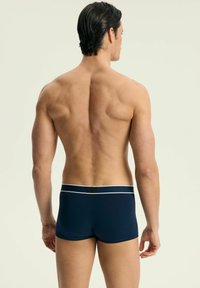 Granatowe kąpielówki z białym pasem, o gładkiej fakturze i dopasowanym kroju, wyświetlane z widoku tylnego na neutralnym tle.