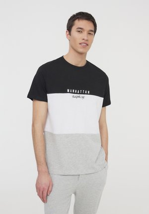 T-shirt color blockato in nero, bianco e grigio, realizzato in un tessuto morbido con collo a giro e maniche corte. Presenta il testo "MANHATTAN" sulla parte anteriore.