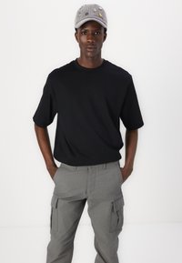 Tricou scurt negru cu mânecă scurtă, asortat cu pantaloni cargo gri, prevăzuți cu buzunare laterale. Capac gri cu desene brodate.