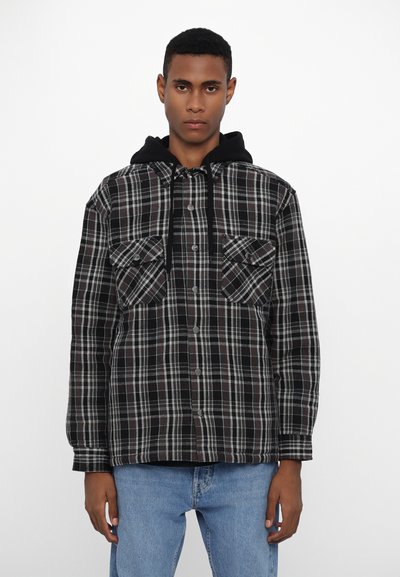 Veste chemise à carreaux noir et gris avec capuche, deux poches poitrine et fermeture à boutons. Tissu doux avec un aspect légèrement texturé.