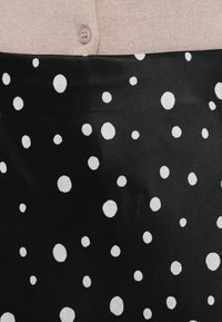 Fekete szövet fehér pöttyökkel, puha kötött rózsaszín felső résszel és gombos záródással. Simogató tapintású, játékos mintázattal.