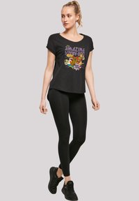 Black t-shirt featuring a colorful "Scooby-Doo" graphic, paired with black leggings and black athletic shoes. Short sleeves, relaxed fit.