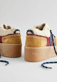 Wildleder-Plattform-Sneaker in Gelb und Bordeaux mit einem flauschigen weißen Innenfutter. Es gibt dekorative Nähte und blaue gemusterte Schnürsenkel.