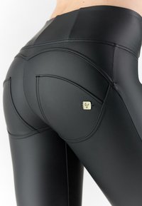 Leggings negros de talle alto hechos de material elástico, con costuras curvas, detalles de bolsillo y un pequeño adorno metálico en la parte trasera.