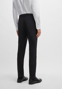 Black dress pants with a slim fit, subtle texture, and back pockets. Worn with a white long-sleeve shirt and black lace-up shoes.