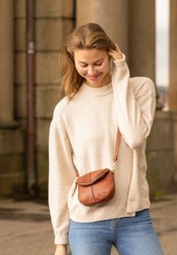 Pull en beige texturé, à coupe ample et avec un col côtelé, associé à un petit sac en cuir marron croisé, rond et muni d'une fermeture éclair.