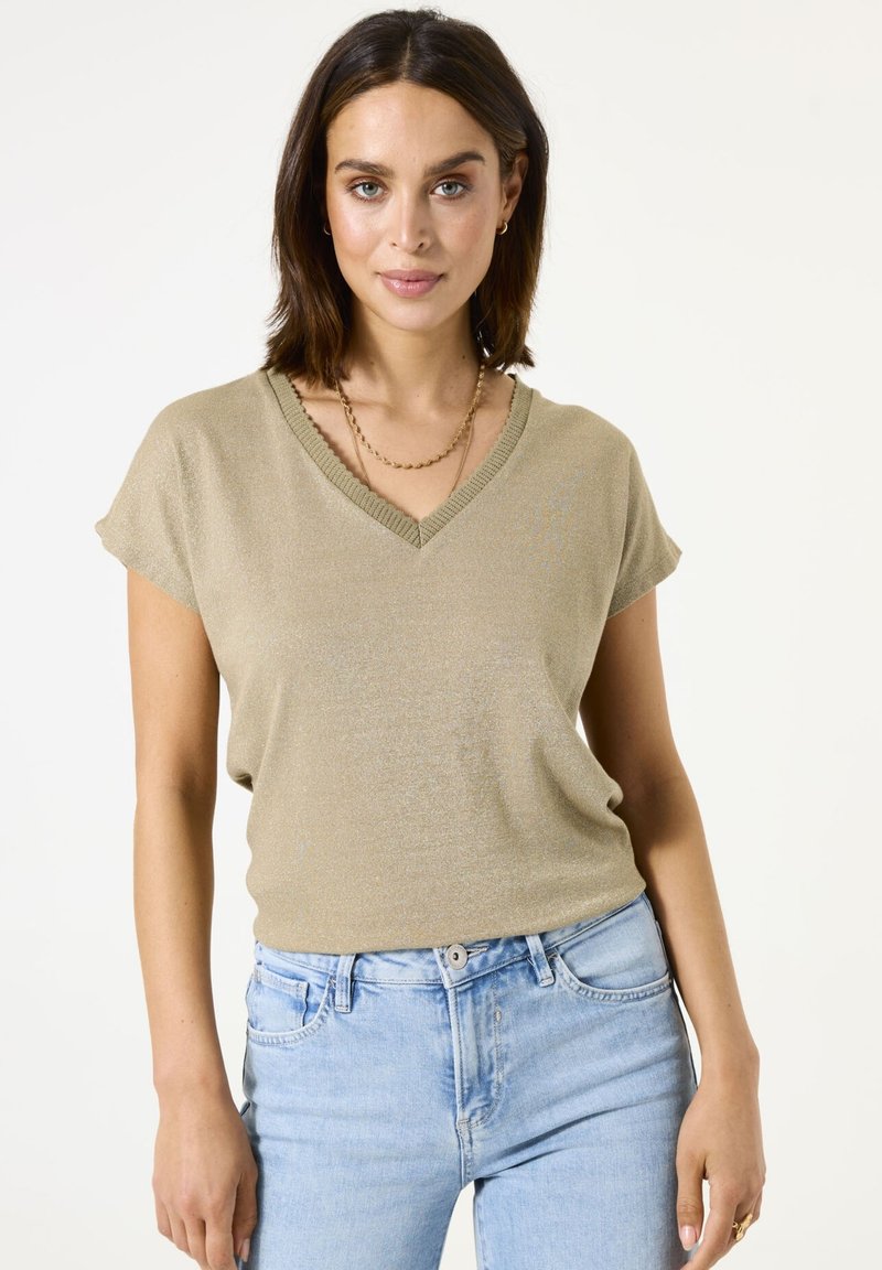 Top de manga corta y cuello en V en verde oliva claro, hecho de un material brillante con una textura suave. Presenta un cuello acanalado y un corte relajado.