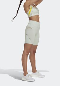 Jasnozielony sportowy krótki top i szorty z wysokim stanem z wycięciami. Białe buty do biegania. Charakteryzuje się czarnymi akcentami i eleganckim designem.