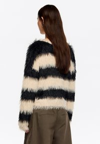 Jersey de lana difusa a rayas con franjas alternas en negro y beige. Mangas largas, escote redondo y tejido suave y texturizado.