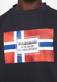 Granatowy sweter z nadrukiem w kształcie prostokąta przedstawiającym norweską flagę z białą ramką oraz napisem "Bądź tym, który wprowadzi zmiany."