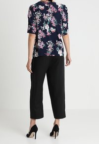 Blusa floreale blu navy con maniche corte, caratterizzata da un design floreale rosa e bianco. Abbinata a pantaloni neri a gamba larga e tacchi alti neri.