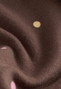 Ruskea, pehmeä kangas, jossa hieman pörröinen pinta ja keltaisia, vaaleanpunaisia sekä vihreitä kukkakuvioita tummalla pohjalla.