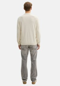 Beige, hosszú ujjú pulóver bordás mandzsettákkal és alsó résszel, szürke farmernadrággal párosítva, egyenes szárú kivágással és hátsó zsebekkel.