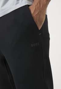 Svarta träningbyxor med en slät textur, utrustade med ficka på sidan och en subtil "BOSS"-logotyp. Designen är strömlinjeformad och tight.