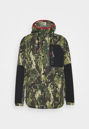 Chaqueta de camuflaje verde y beige con parches negros en los codos, bolsillo en el pecho negro con cremallera, capucha forrada de rojo y cierre frontal con botones.