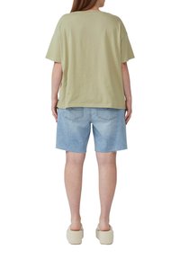 Hellgrünes, übergroßes Baumwoll-T-Shirt kombiniert mit Denim-Shorts, die einen fransigen Saum und Gesäßtaschen haben. Getragen mit beigen Plateau-Slippern.