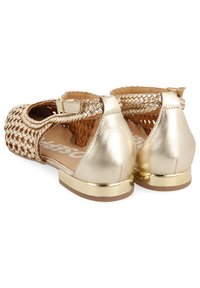 Sandales de couleur or avec un dessus tissé, design ouvert et accents métalliques décoratifs sur le talon. Semelle plate, bride de cheville réglable.