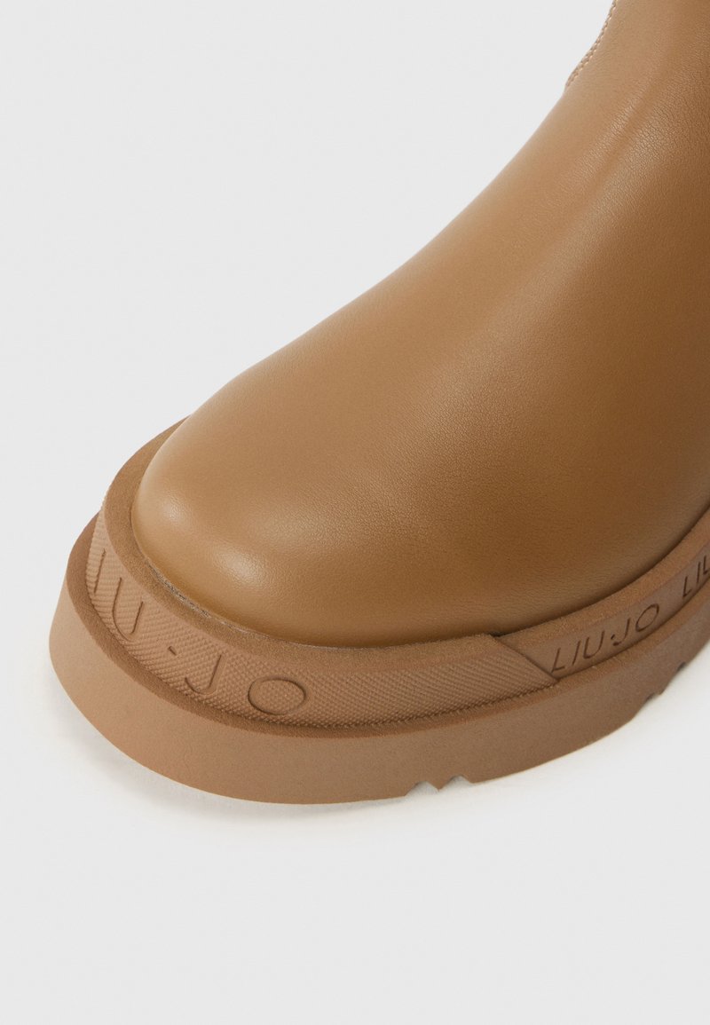 Braunes Lederknöchelboot mit abgerundeter Zehe, ausgestattet mit einer strukturierten Gummisohle und einem reliefierten Logo-Detail an der Seite. Glatte Oberfläche.