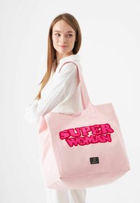 Sac fourre-tout en toile rose avec un design flou en rose "SUPER WOMAN". Le sac possède des anses robustes et une forme carrée, adapté à divers usages.